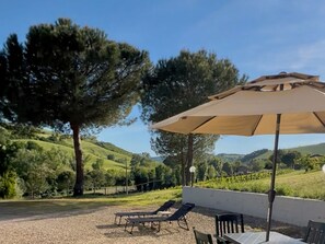 A patio with outdoor seating, a large umbrella, and a view of rolling hills. - Dolce Collina Holiday Home,
Sunset terrace & vineyard views, near Bologna/Imola (Dozza)