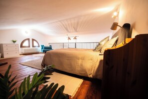 Ein Schlafzimmer mit Holzboden, einem Bett mit beige farbenem Überwurf, einem Schminktisch, einem Heizkörper und einem Fenster mit gebogenem Design.