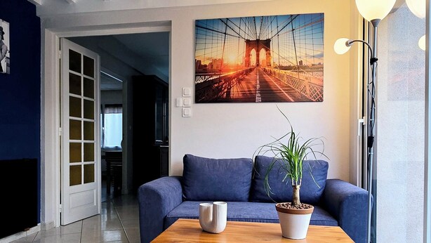 A modern living room with a blue sofa, a wooden coffee table, and a large painting of a bridge. - Appt, with private outdoor space with barbecue, swimming pool (Aigueperse)