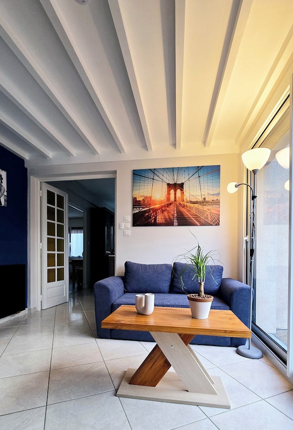 A modern living room with a blue sofa, a wooden coffee table, and a large painting of a bridge. - Appt, with private outdoor space with barbecue, swimming pool (Aigueperse)