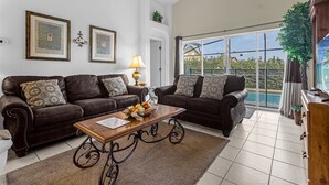 A living room with two dark brown leather sofas, a wooden coffee table, and a large window offering a view of a residential area. - Delightful Family Pool Villa in Glenbrook with 4 Bedrooms & 3 Bathrooms (Clermont)