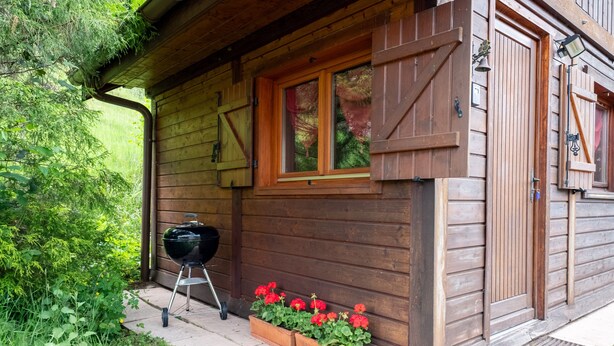 Une cabane en bois avec une fenêtre, un barbecue et des jardinières.