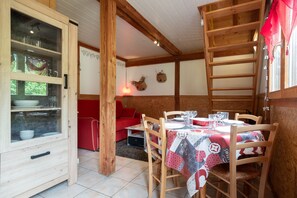 Un comedor con una mesa preparada para cuatro personas, sillas de madera, un sofá rojo y un armario con puertas de cristal.