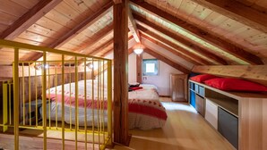 Une chambre mansardée avec de hauts plafonds, un lit superposé, une petite fenêtre et des poutres en bois.