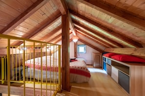 Un dormitorio abuhardillado con techos altos, una cama litera, un ventanal pequeño y vigas de madera.