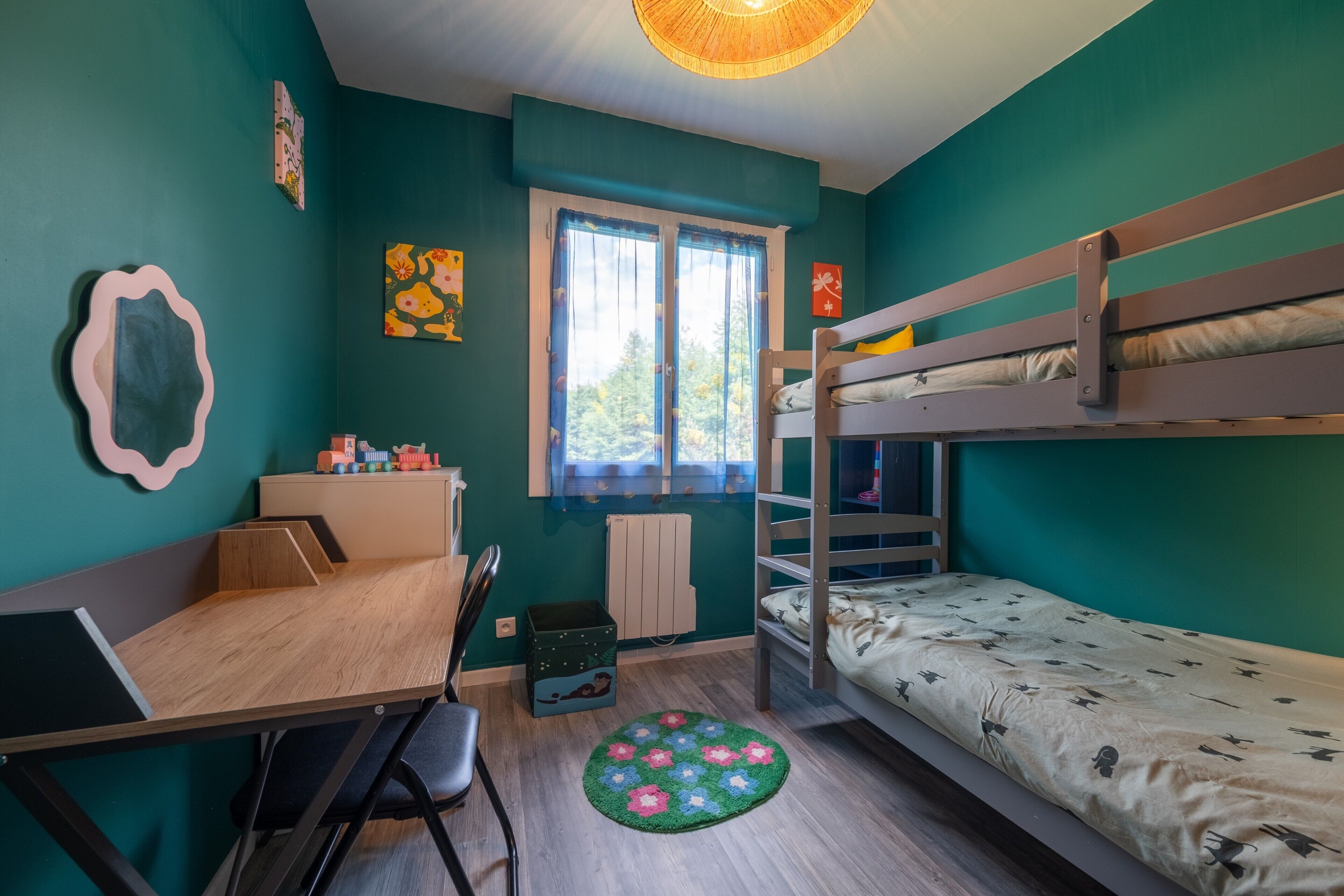 A room with a bunk bed, a desk with a chair, a radiator, and a window with curtains.