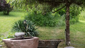 Un jardin avec une fontaine en pierre, un mur en pierre et un arbre.