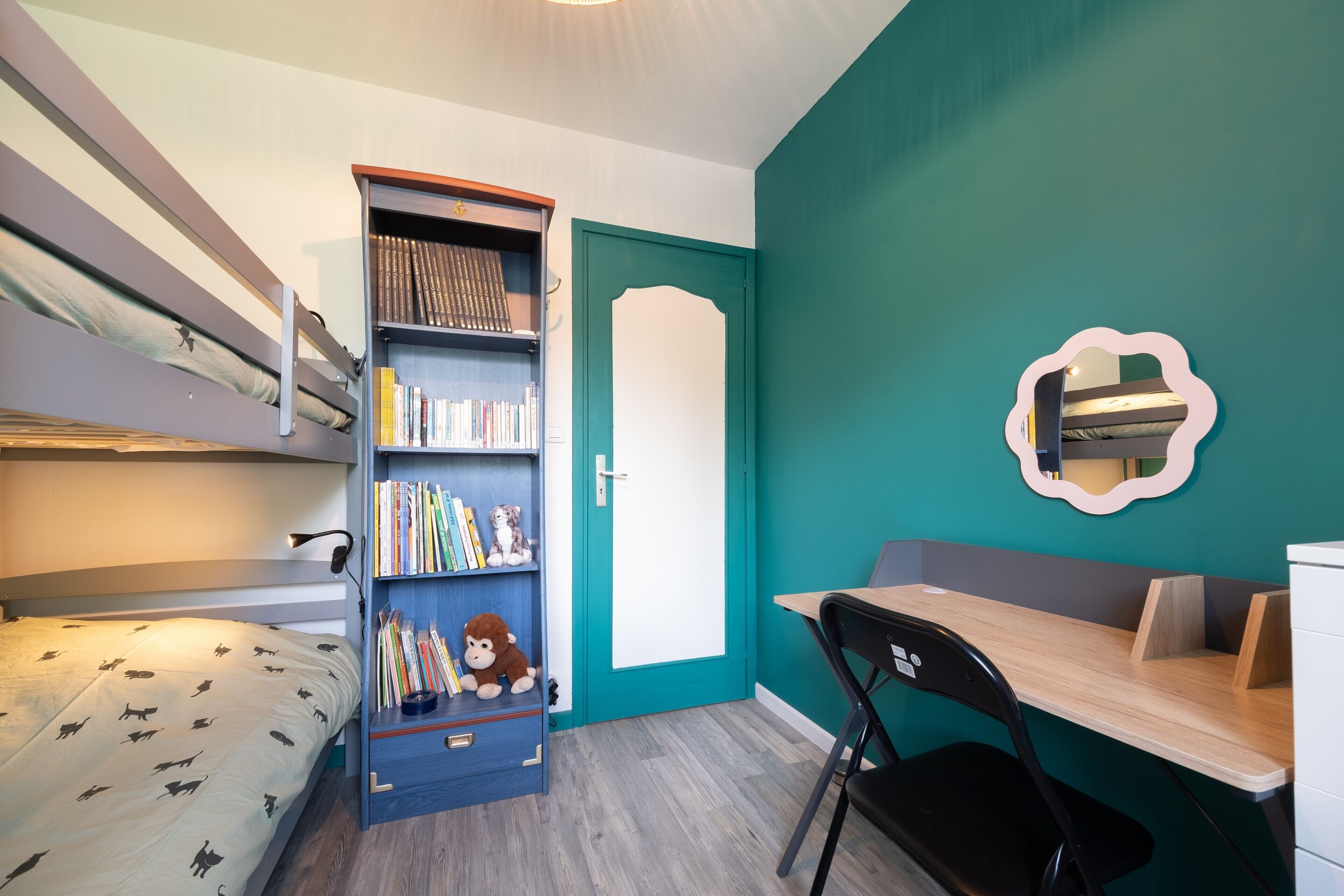 A room with bunk beds, a desk, a chair, a bookshelf, and a door.