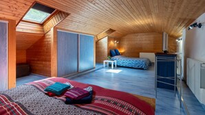 Un intérieur en bois avec un plafond en pente, un lit avec une literie à motifs, une petite table et un radiateur.