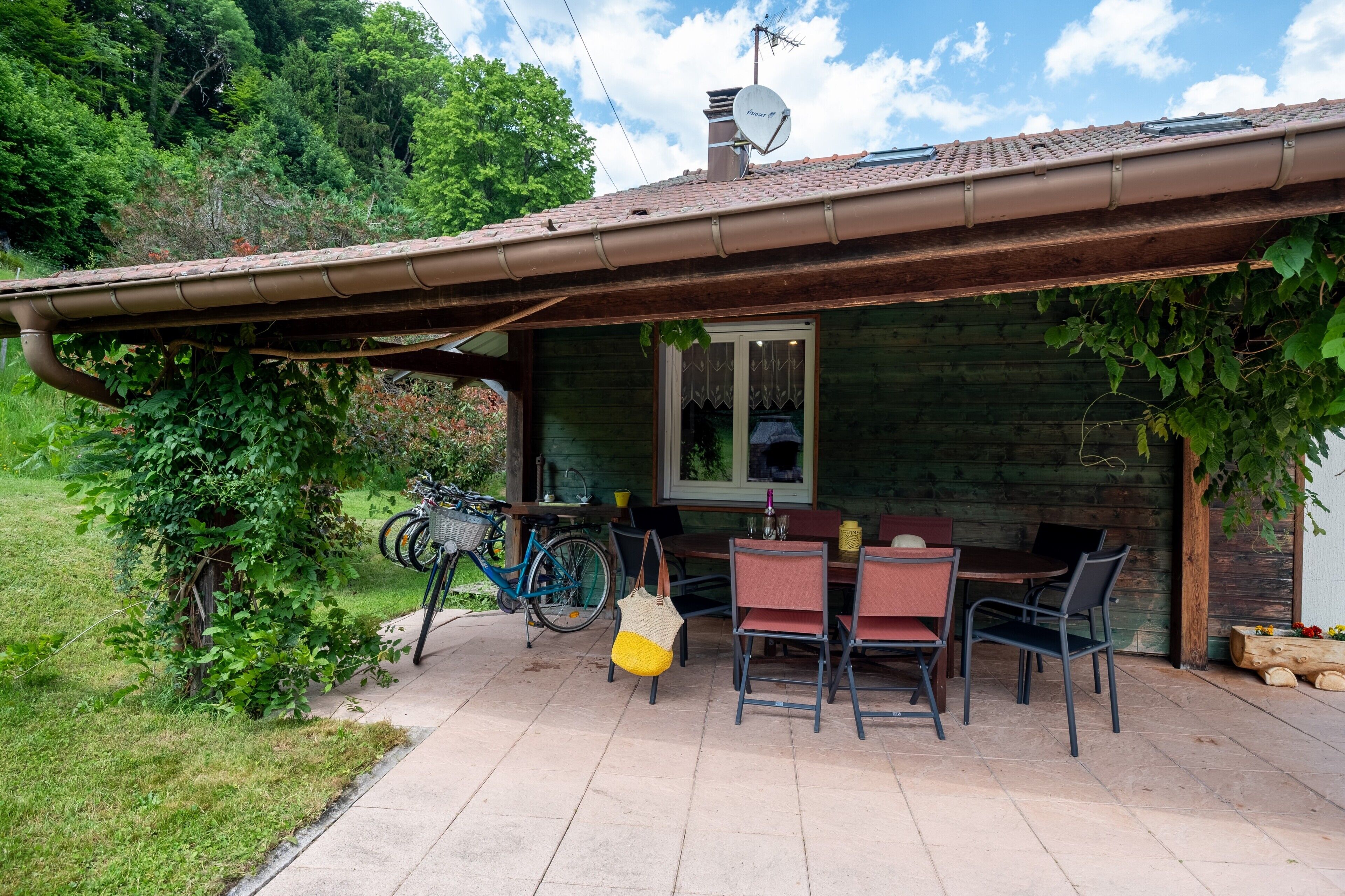 A wooden cabin with a covered patio, a dining table with chairs, and a bicycle.