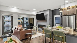 A modern kitchen with a flat-screen TV, a fireplace, and a dining area with bar stools. - New Luxury 3 bedroom (Canmore)