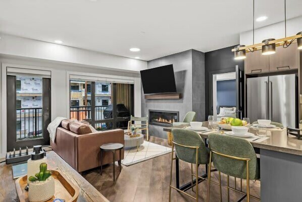 A modern kitchen with a flat-screen TV, a fireplace, and a dining area with bar stools.