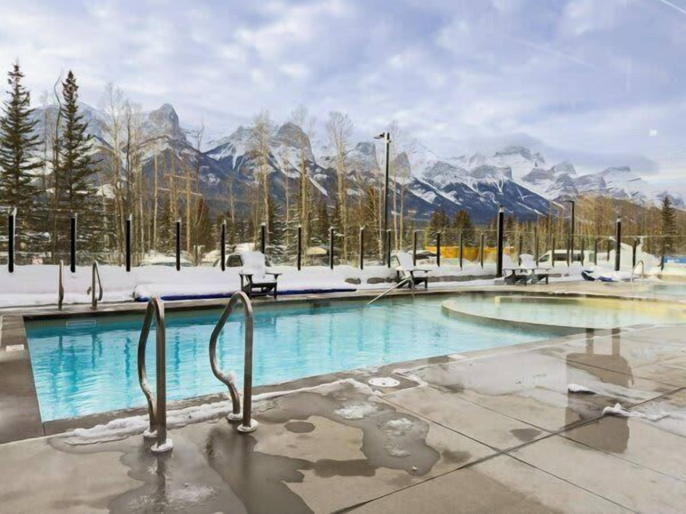 A pool area with a view of snow-covered mountains and trees.