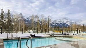 A pool area with a view of snow-covered mountains and trees. - New Luxury 3 bedroom (Canmore)