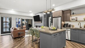 A modern kitchen with grey cabinets, a central island, and a dining area with a sofa and chairs. - New Luxury 3 bedroom (Canmore)