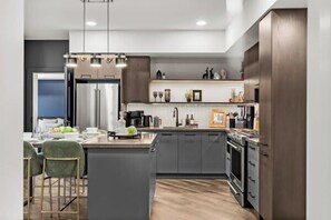 A modern kitchen with dark cabinets, a central island, and a dining area with green chairs.