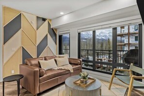 A modern living room with a brown leather sofa, a round coffee table, and a view of mountains through large windows.