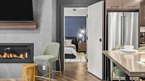 A modern hotel room with a fireplace, a dining area, and a kitchen. - New Luxury 3 bedroom (Canmore)
