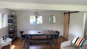 Un área de comedor con una mesa y sillas de madera, una estantería, un espejo y una ventana con vistas al exterior.