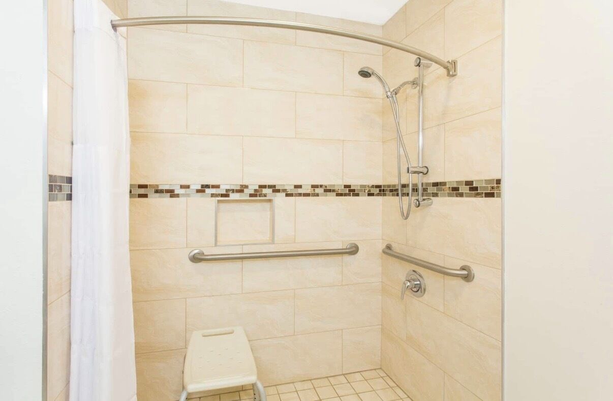 A small, enclosed shower area with a grab bar, a bench, and a tiled floor.
