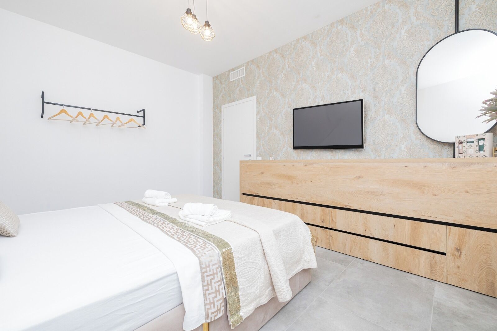 A modern bedroom with a bed, a wooden dresser, a flat-screen TV, and a mirror.