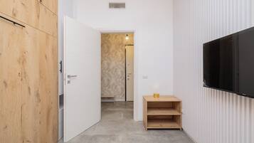 Een gang met een houten garderobe, een witte deur, een klein houten tafeltje en een tv aan de muur.
