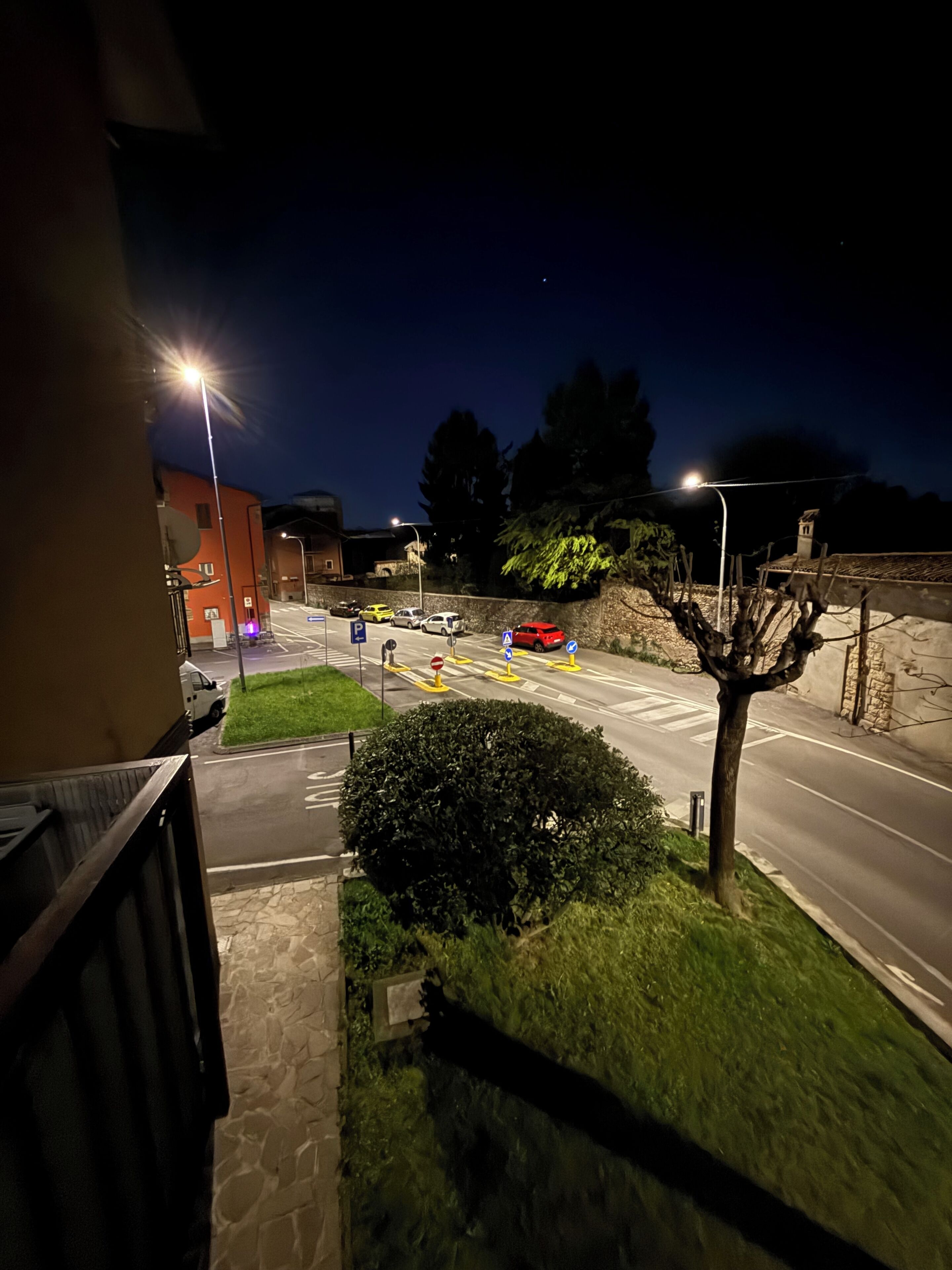 Una vista notturna di una strada con auto, lampioni e un edificio con una parete in pietra.