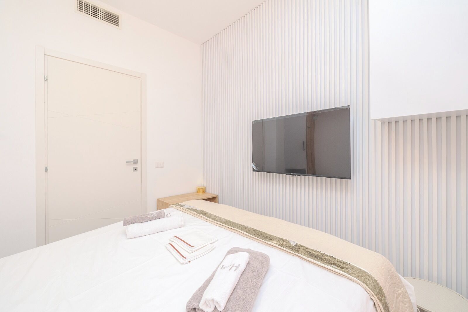 A hotel room with a bed, a TV mounted on the wall, and a door.