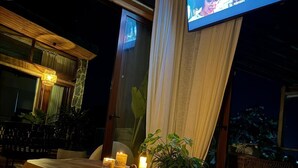 Ein gemütlicher Sitzbereich im Innenbereich mit einem Holztisch, Kissen und einem Fernseher, der ein Programm zeigt.