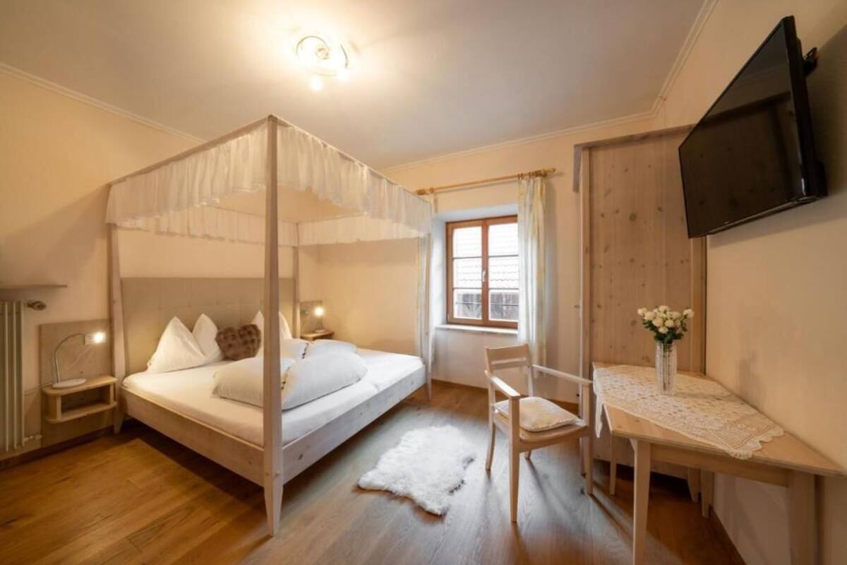 Une chambre à coucher avec un lit à baldaquin, un bureau avec une chaise, une télévision et une fenêtre avec des rideaux.