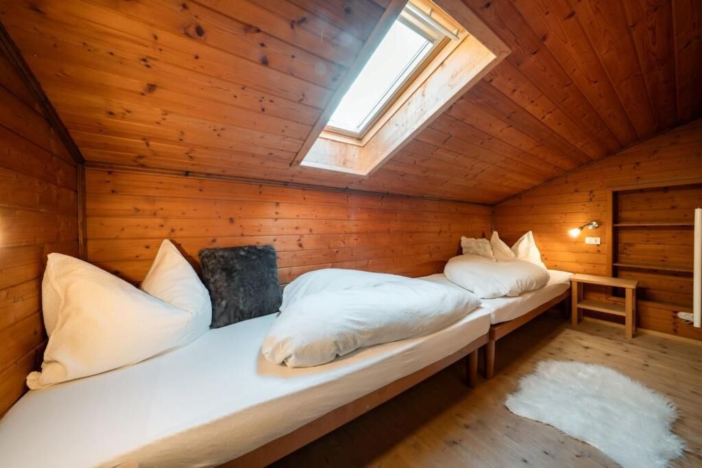 A wooden cabin with a loft bed, a skylight, and a small bedside table.