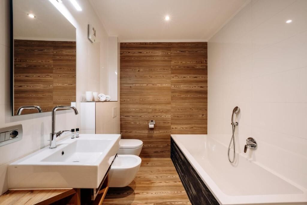A modern bathroom with a wooden wall, a white sink, a toilet, and a bathtub.