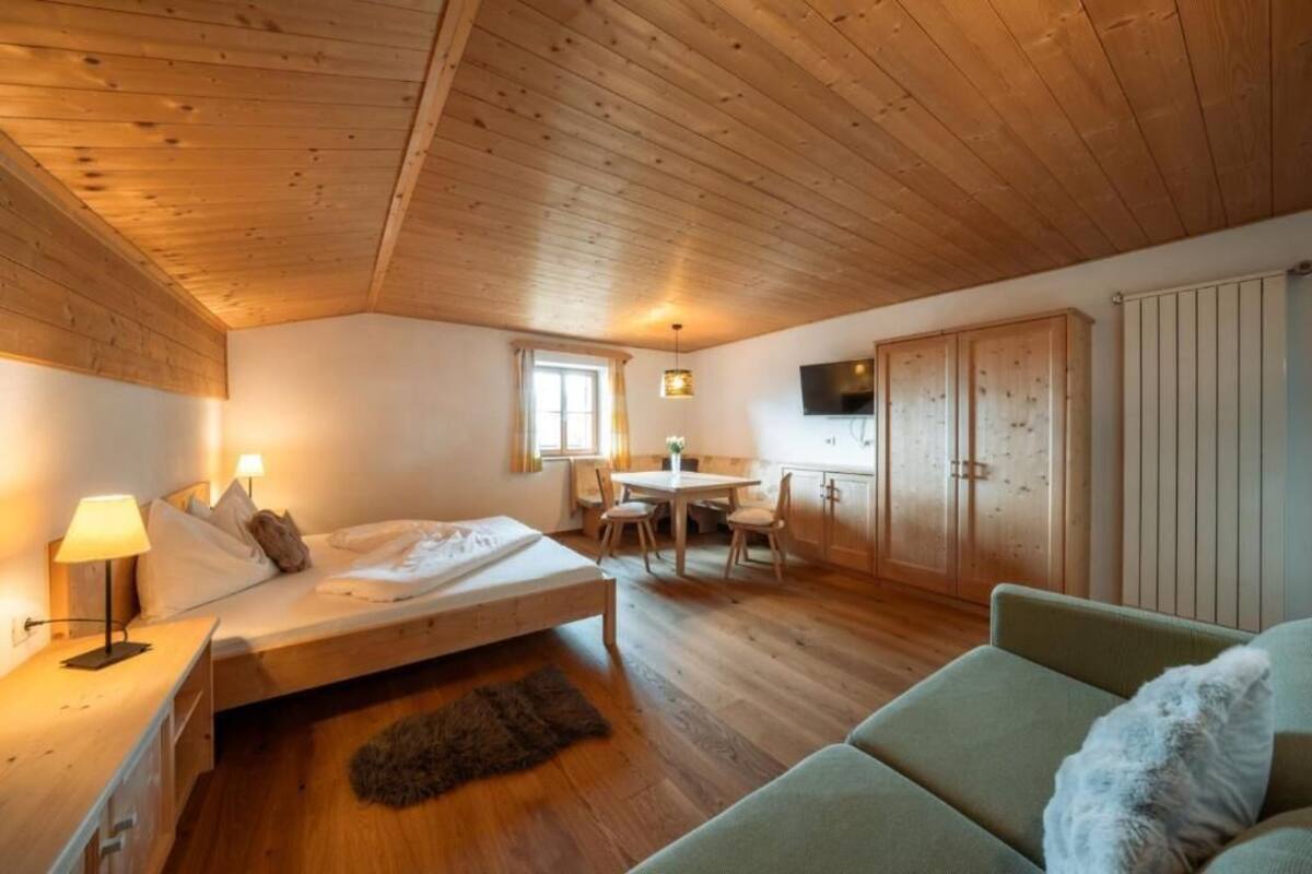 Une pièce comprenant un lit, un canapé vert, un plafond en bois, une table à manger avec des chaises et un téléviseur fixé au mur.