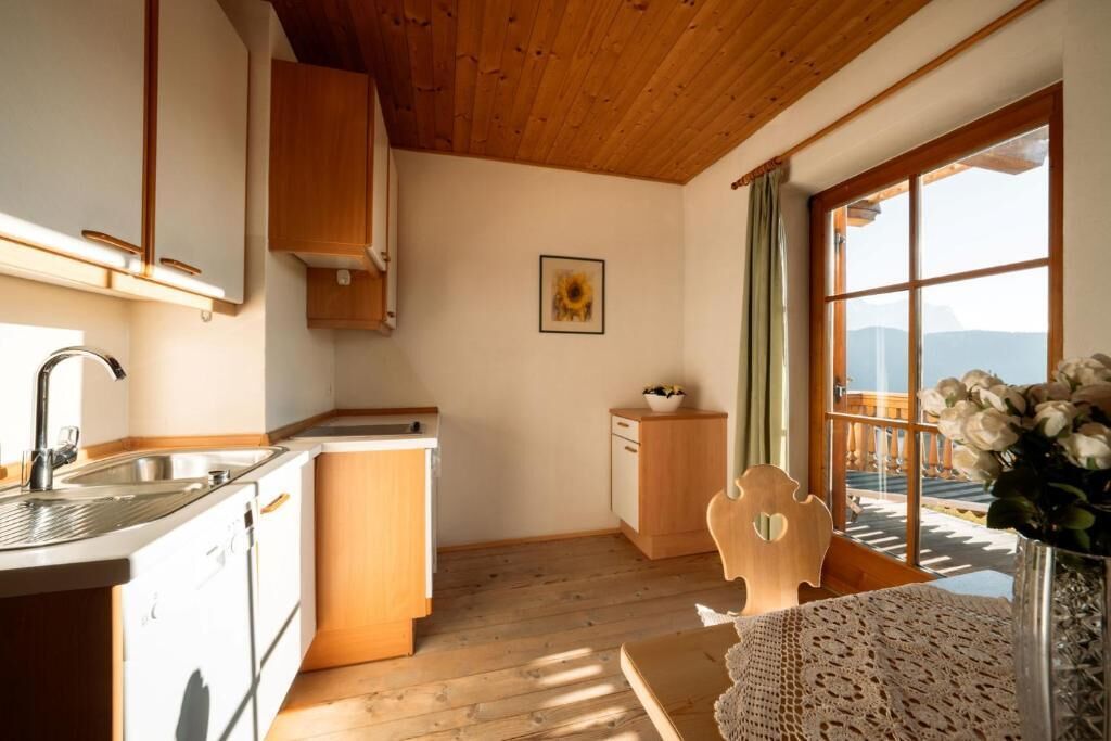 Une cuisine avec des meubles de rangement en bois, un évier et une fenêtre donnant sur un balcon.