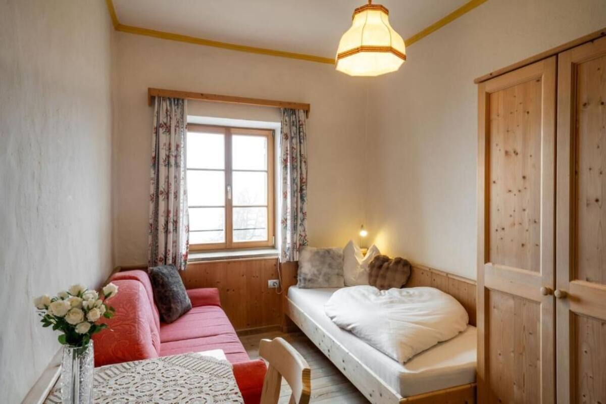 Une pièce comprenant un lit, un canapé, une table avec un vase, une fenêtre avec des rideaux et une armoire en bois.