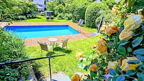 A backyard with a swimming pool, a wooden deck, and a garden with roses. - Garni Tschutscherhof (Laion)