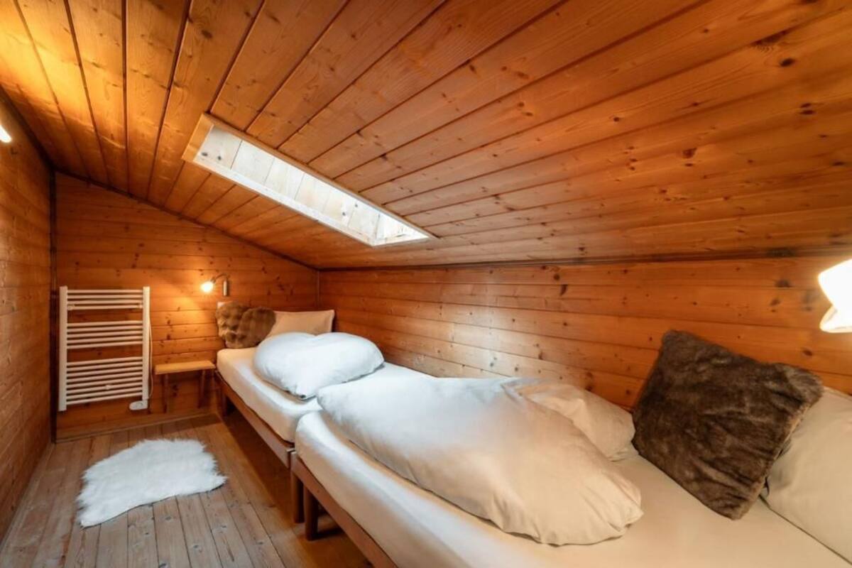 Une pièce chaleureuse dans un chalet, avec des murs en bois, un plafond en pente, un puits de lumière, un lit avec des oreillers, un banc et un tapis en fourrure.