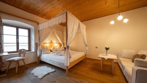 A bedroom with a four-poster bed, a wooden ceiling, a small table with a vase, and a sofa. - Garni Tschutscherhof (Laion)