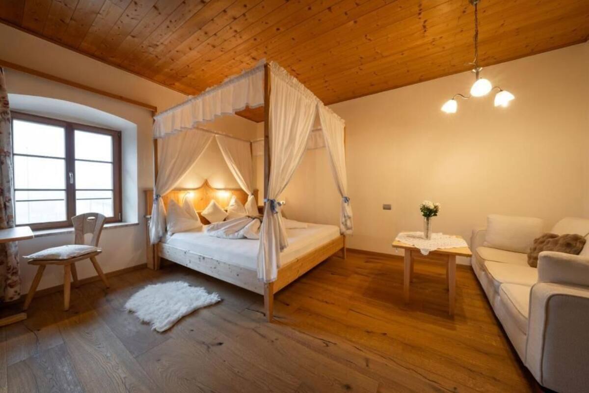 Une chambre à coucher avec un lit à baldaquin, un plafond en bois, une petite table sur laquelle est posé un vase, et un canapé.