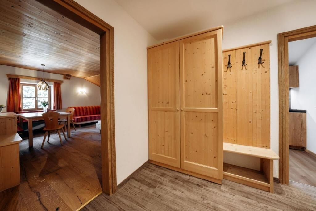 Ein Zimmer mit Holzboden, einem Essbereich mit Tisch und Stühlen, einer Bank und einem Schrank mit Haken.