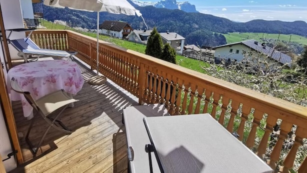 A wooden deck with a table and chairs, a white umbrella, and a view of mountains and houses. - Garni Tschutscherhof (Laion)