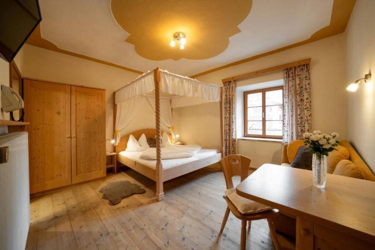 Une chambre à coucher avec un lit à baldaquin, une armoire en bois, une table à manger ornée d’un vase de fleurs et une fenêtre avec des rideaux.
