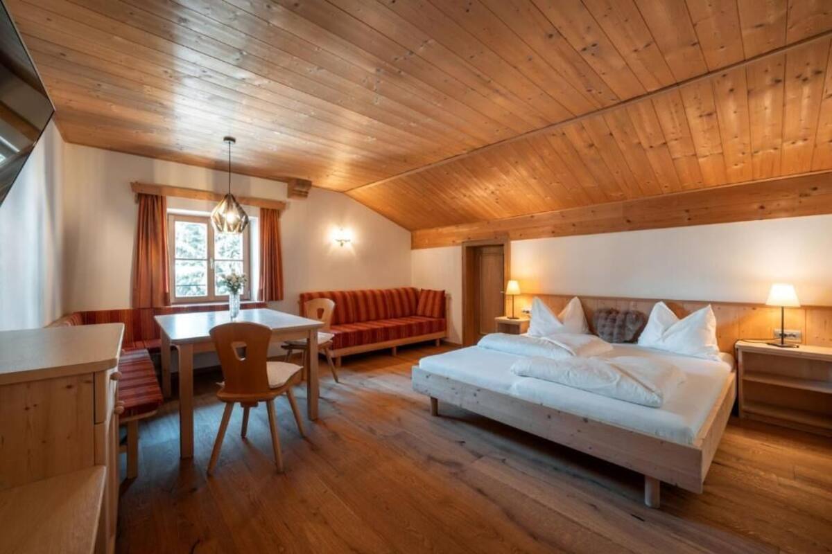 Une pièce avec un plafond en bois, un lit, un canapé, une table avec des chaises et une fenêtre avec des rideaux.