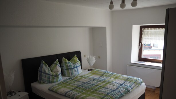 Une chambre à coucher avec un lit, une table de chevet, une fenêtre donnant sur un paysage agréable et un radiateur.