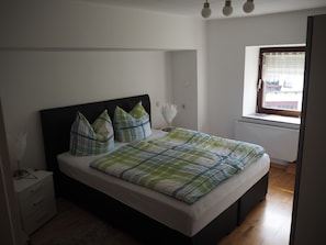 Une chambre à coucher avec un lit, une table de chevet, une fenêtre donnant sur un paysage agréable et un radiateur.