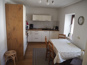 Une cuisine compacte avec des meubles blancs, une table à manger recouverte d’une nappe à motifs et une chaise en bois.