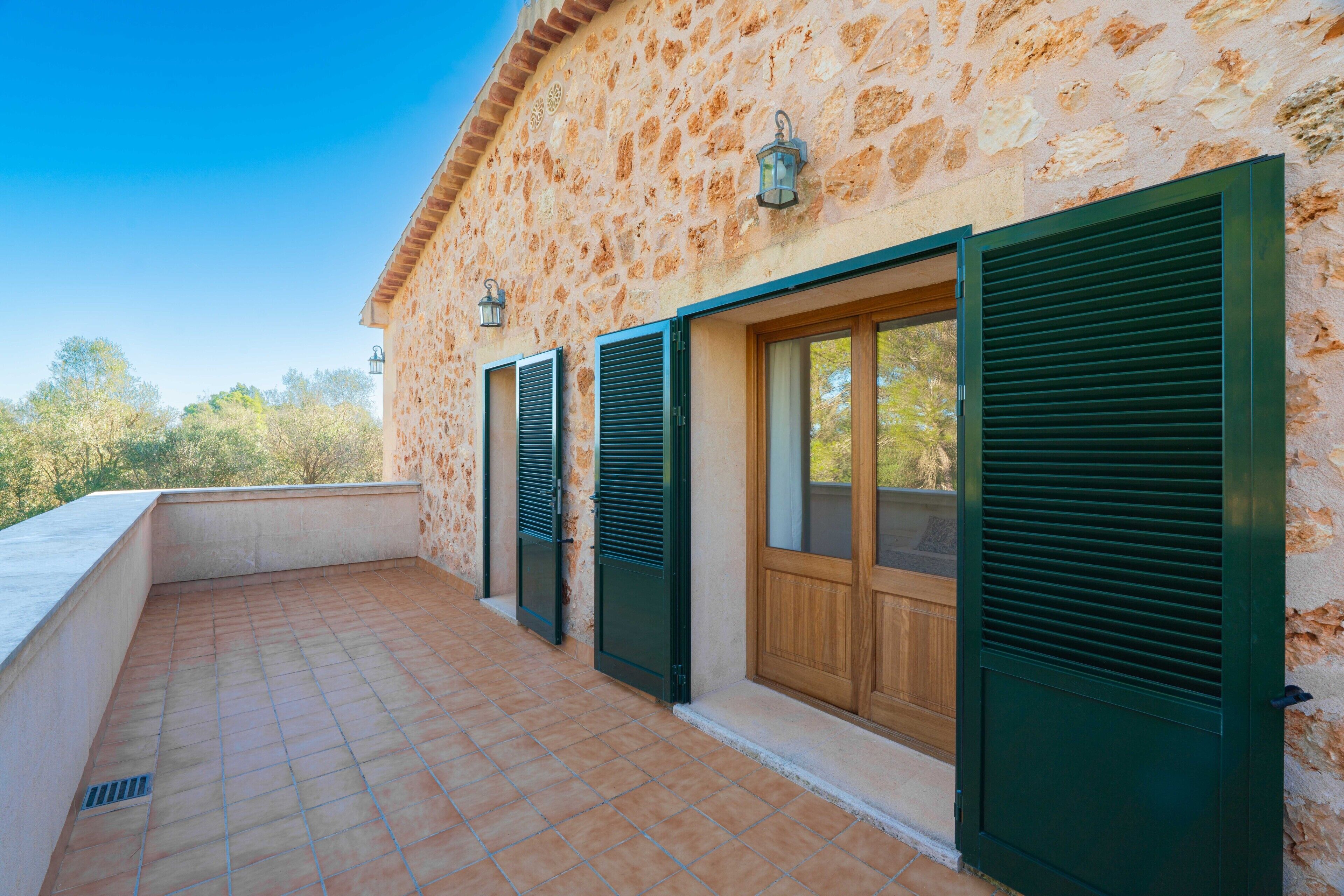 A building with stone walls, green shutters, and a tiled terrace.