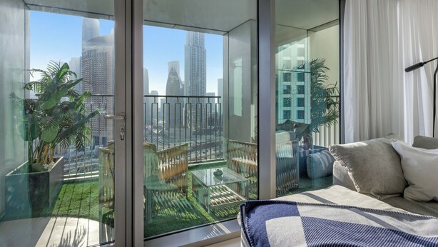 Een moderne hotelkamer met een ruim balkon, een glazen deur, een zithoek en uitzicht op de stad.