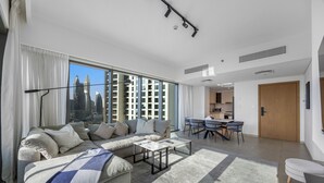 Een moderne woonkamer met een modulaire bank, een eethoek en uitzicht op de stad door grote ramen.