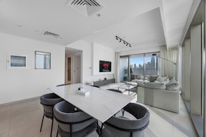 A modern living room with a dining area, a large TV, and a city view. - Burj Khalifa View l Pool, Gym & Downtown Ease (Zaa'beel Second)